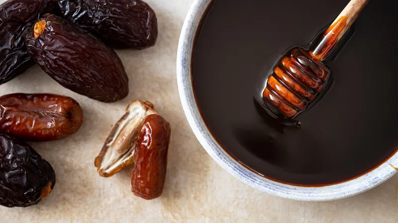 Natural Iranian date syrup in a bowl with fresh date beside it, showcasing its rich dark color and thick texture – NOV Export premium date syrup product